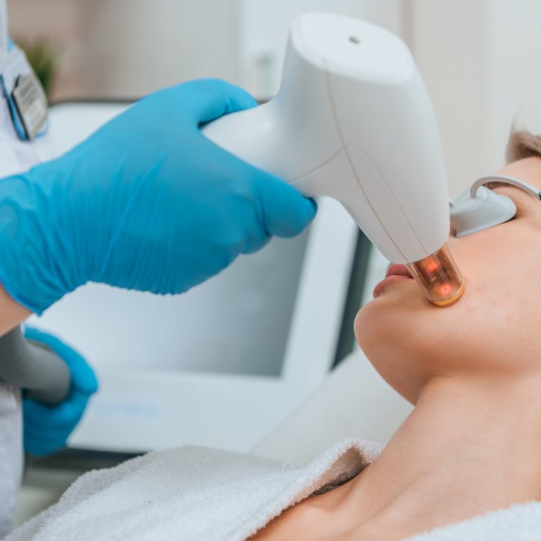Blonde girl in protective goggles receiving laser treatment in clinic